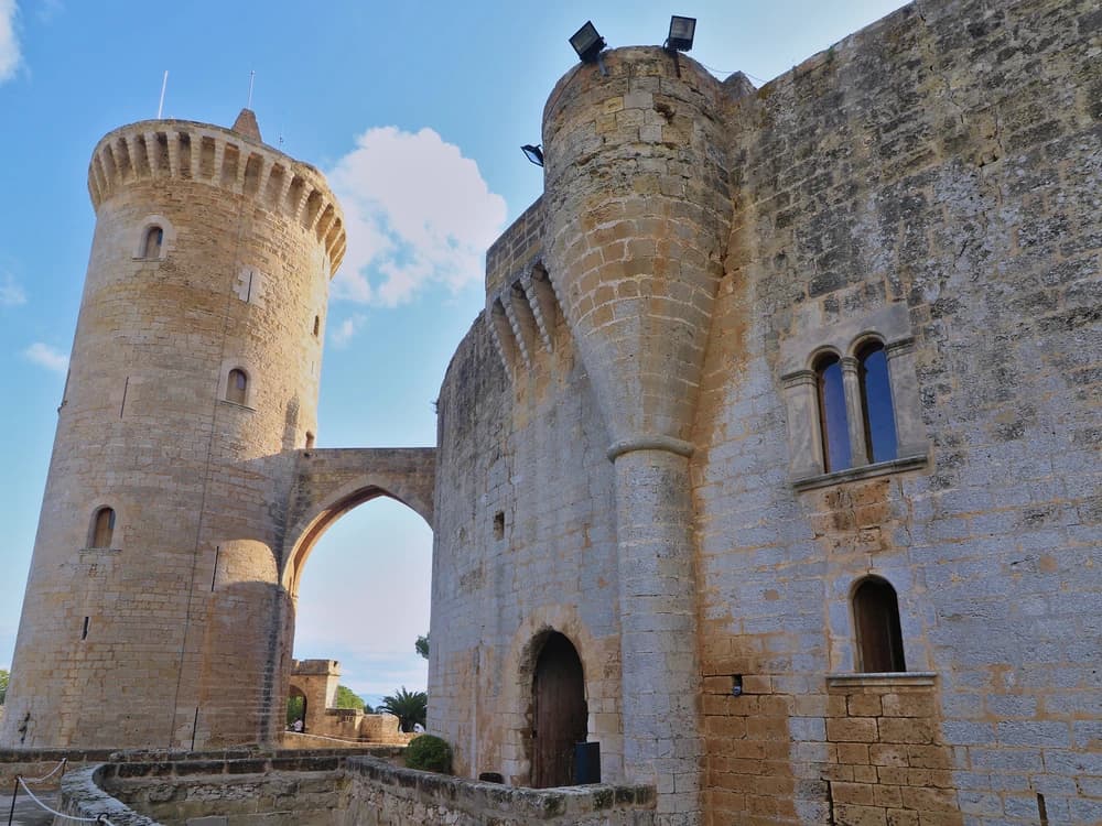 Bellver Castle's perfectly circular Gothic form rising from pine-forested hillside above Palma de Mallorca, with the Bay of Palma shimmering in the distance