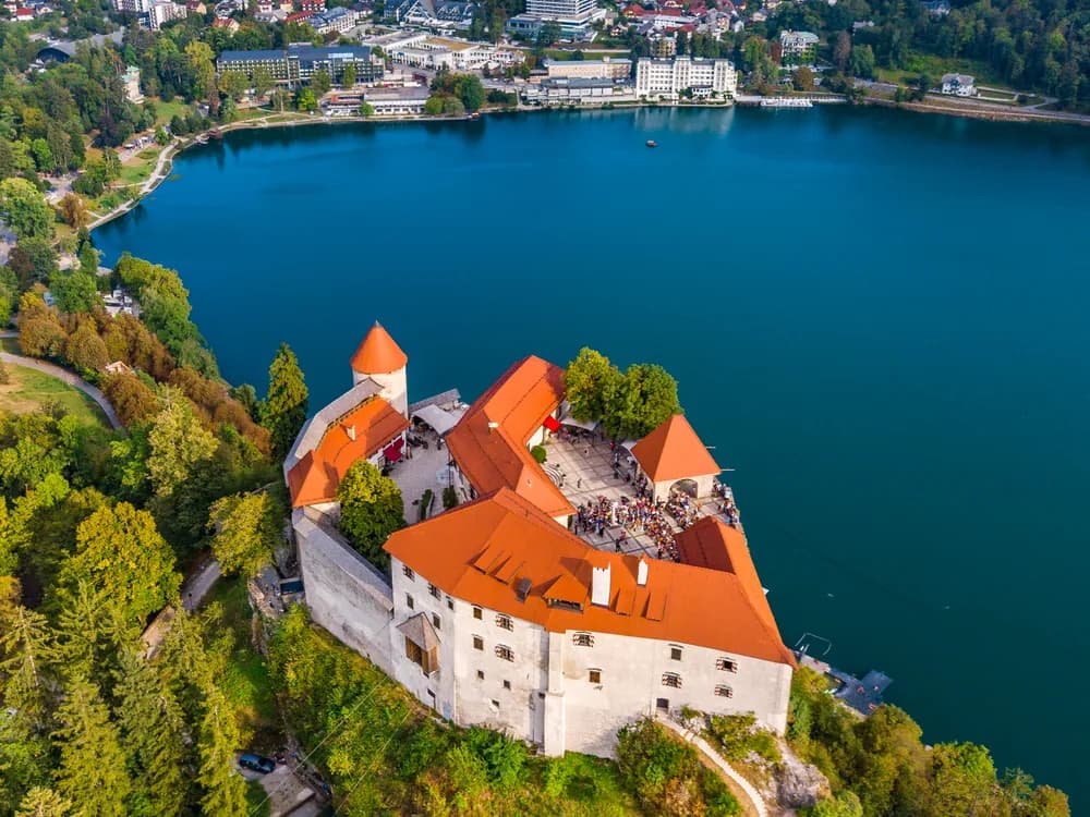 Bled Castle on its sheer cliff above the emerald waters of Lake Bled with the Julian Alps behind, Slovenia