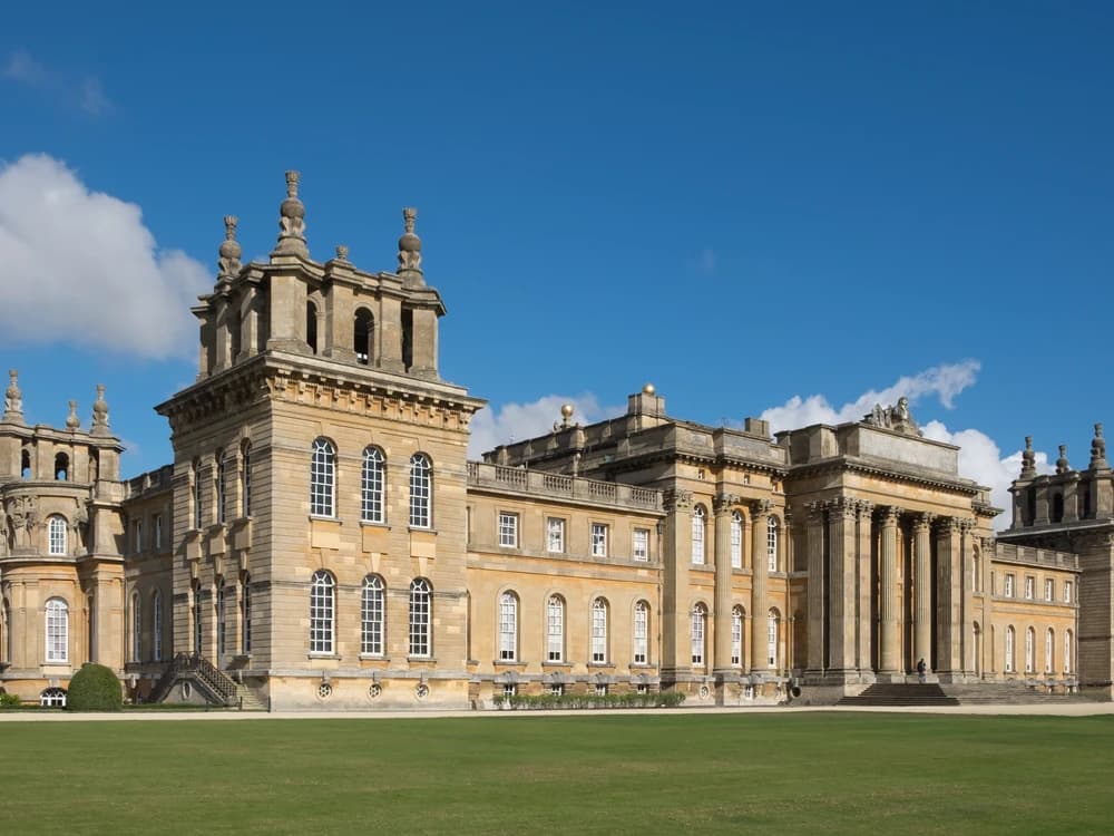 Blenheim Palace's grand Baroque façade reflected in Capability Brown's great lake, with the Column of Victory rising above ancient oaks on a summer afternoon
