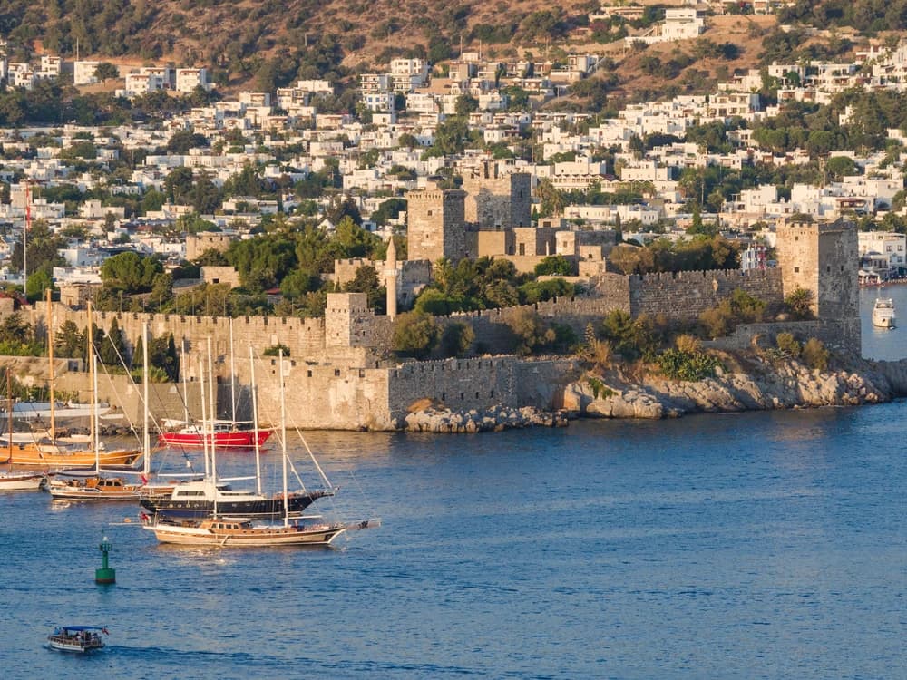 Bodrum Castle and its five towers reflected in the Aegean harbour of Bodrum, Turkey, with the Greek island of Kos visible beyond