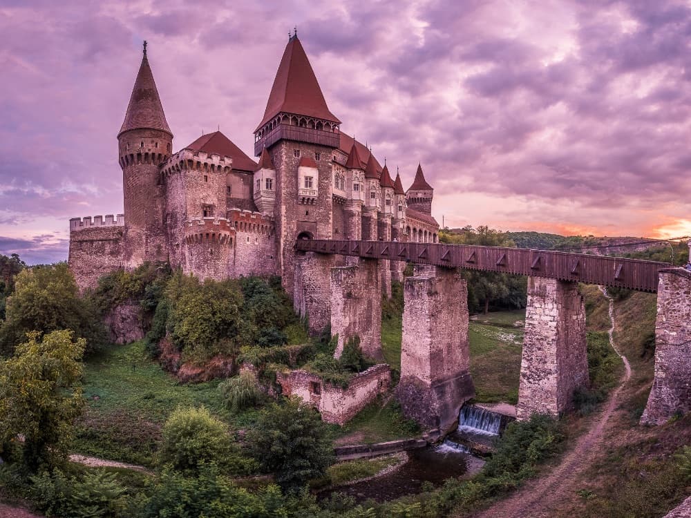 Corvin Castle in Hunedoara, Transylvania — Gothic towers and drawbridge rising dramatically above the Zlasti river