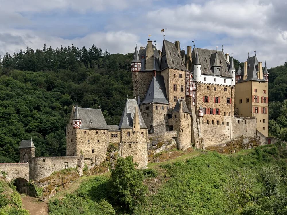 Burg Eltz rising from the forested Moselle Valley hills in morning mist