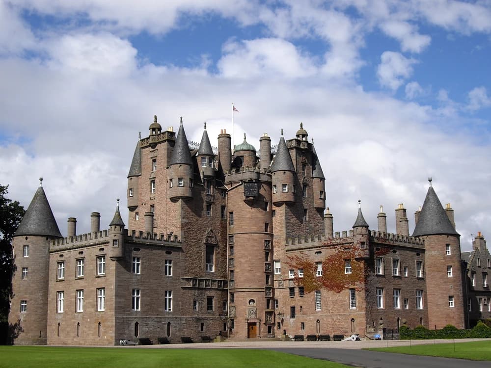 Glamis Castle's Scottish Baronial towers and conical turrets rising above a tree-lined avenue in Angus on a clear summer morning