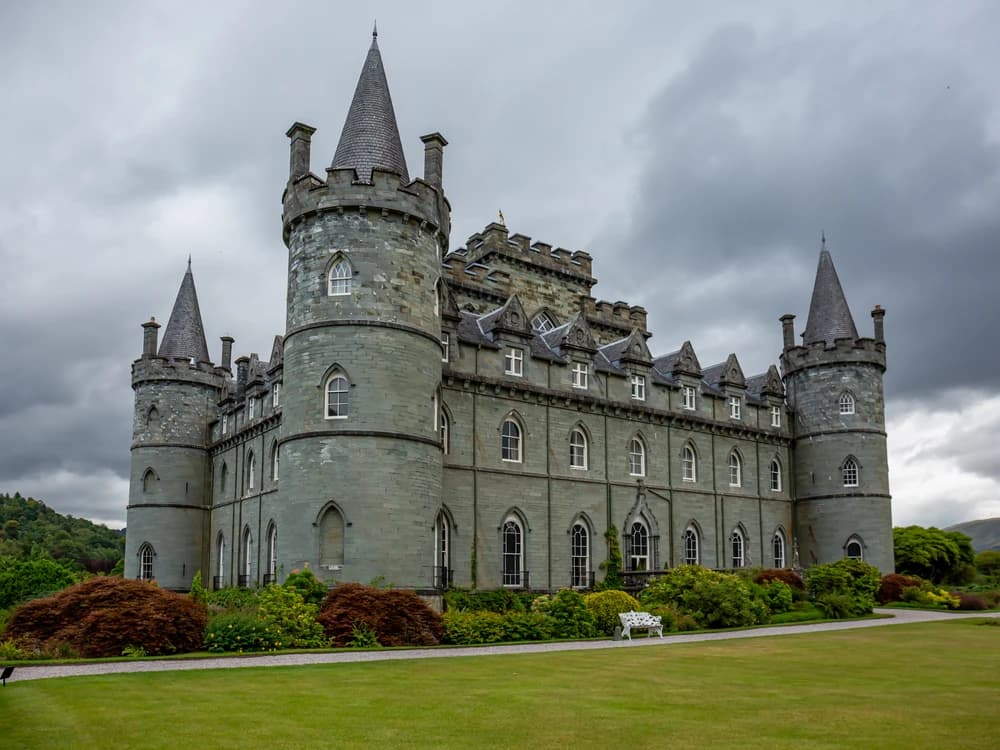 Inveraray Castle's iconic blue-grey turreted facade reflected in the River Aray, surrounded by woodland in Argyll on a still autumn day