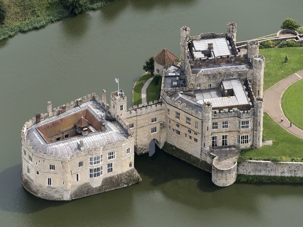 Leeds Castle rising from its shimmering moat in the Kent countryside, the stone towers perfectly reflected in still water on a sunny morning