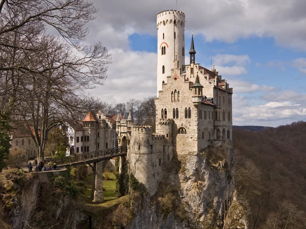 Lichtenstein Castle's slender Neo-Gothic tower rising dramatically from a sheer limestone cliff in the Swabian Alps of Baden-Württemberg, surrounded by autumn forest
