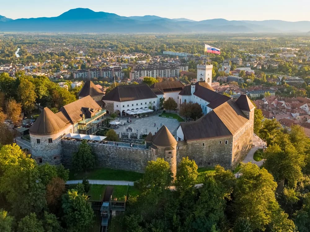 Ljubljana Castle on its wooded hill above the orange rooftops of the old town at dusk