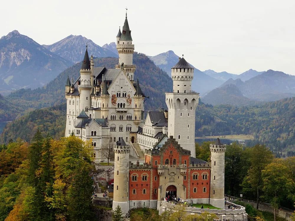 Neuschwanstein Castle rising above the Bavarian forest with snow-capped Alps in the background