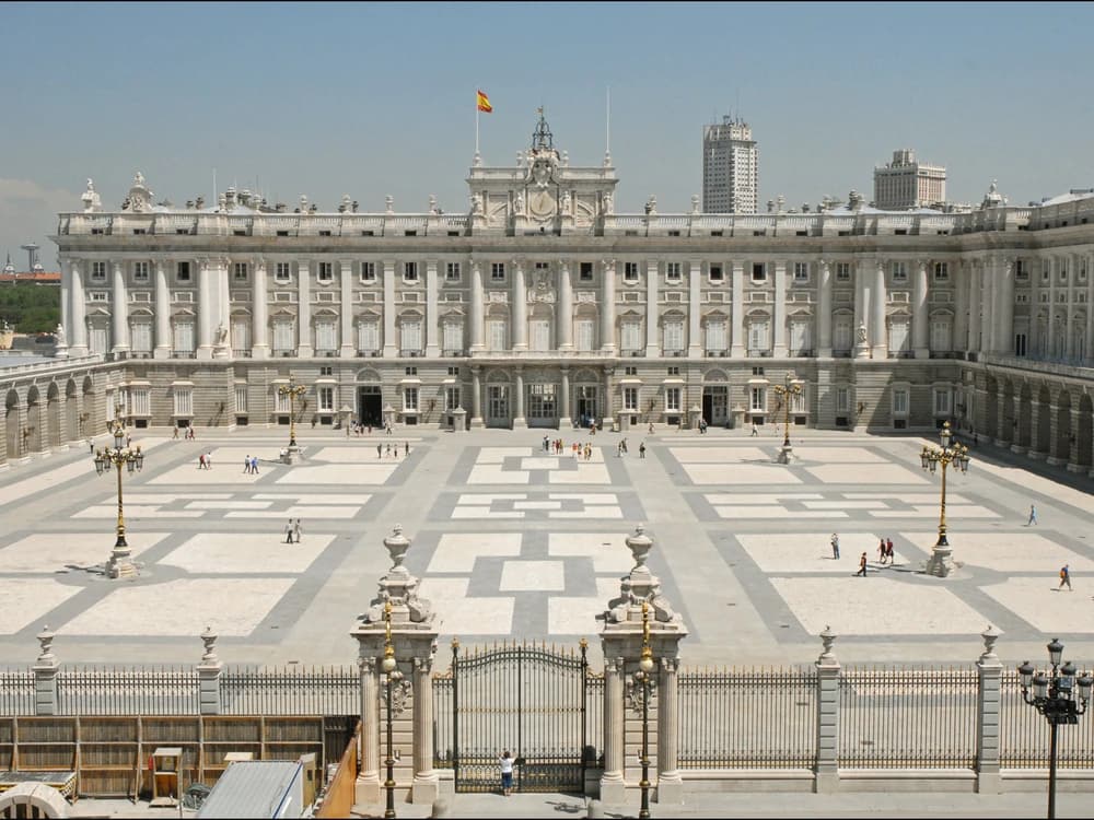 The neoclassical facade of the Royal Palace of Madrid seen from the Plaza de la Armería with the Almudena Cathedral behind