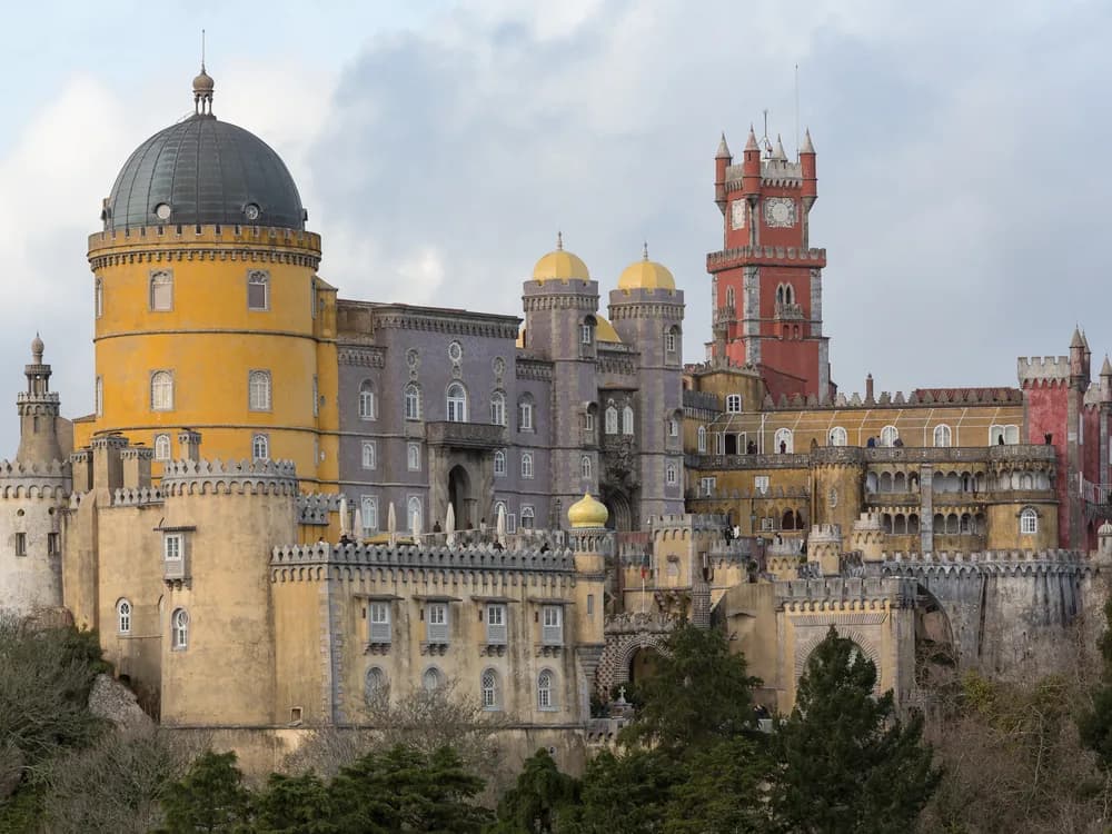 Pena Palace in vivid yellow and red above the misty forests of Sintra at dawn