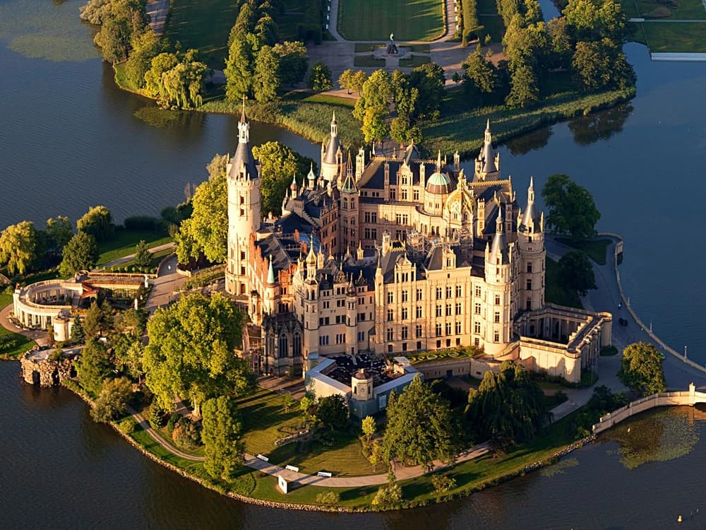 Schwerin Castle rising from its island in Lake Schwerin, its 86 spires and towers perfectly reflected in the still water on a clear morning