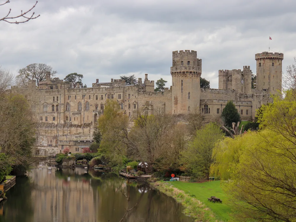 Warwick Castle's medieval towers reflected in the River Avon on a clear morning